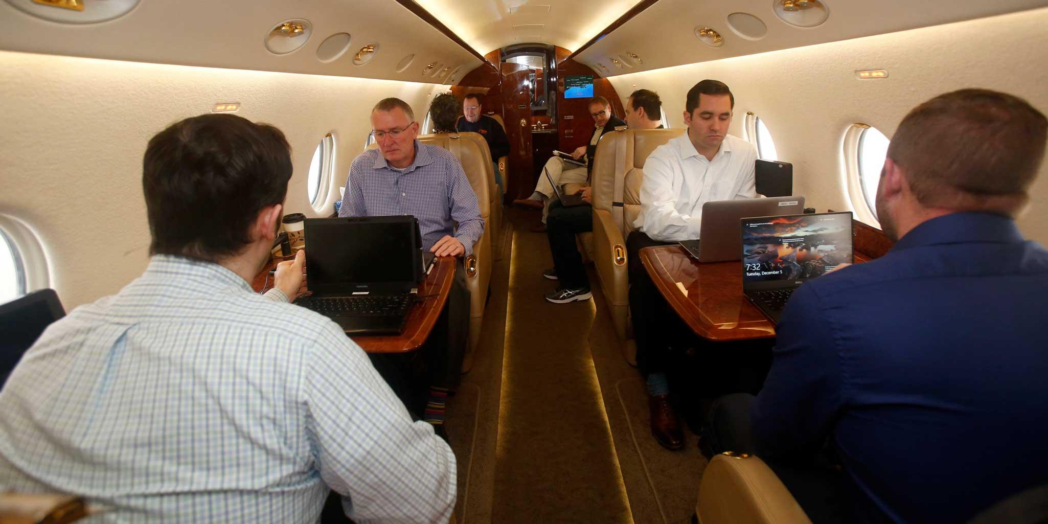 men on laptops inside of a business jet