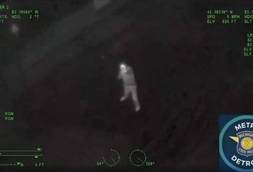 night vision mode view of man on ground pointing long gun at Michigan State Police helicopter